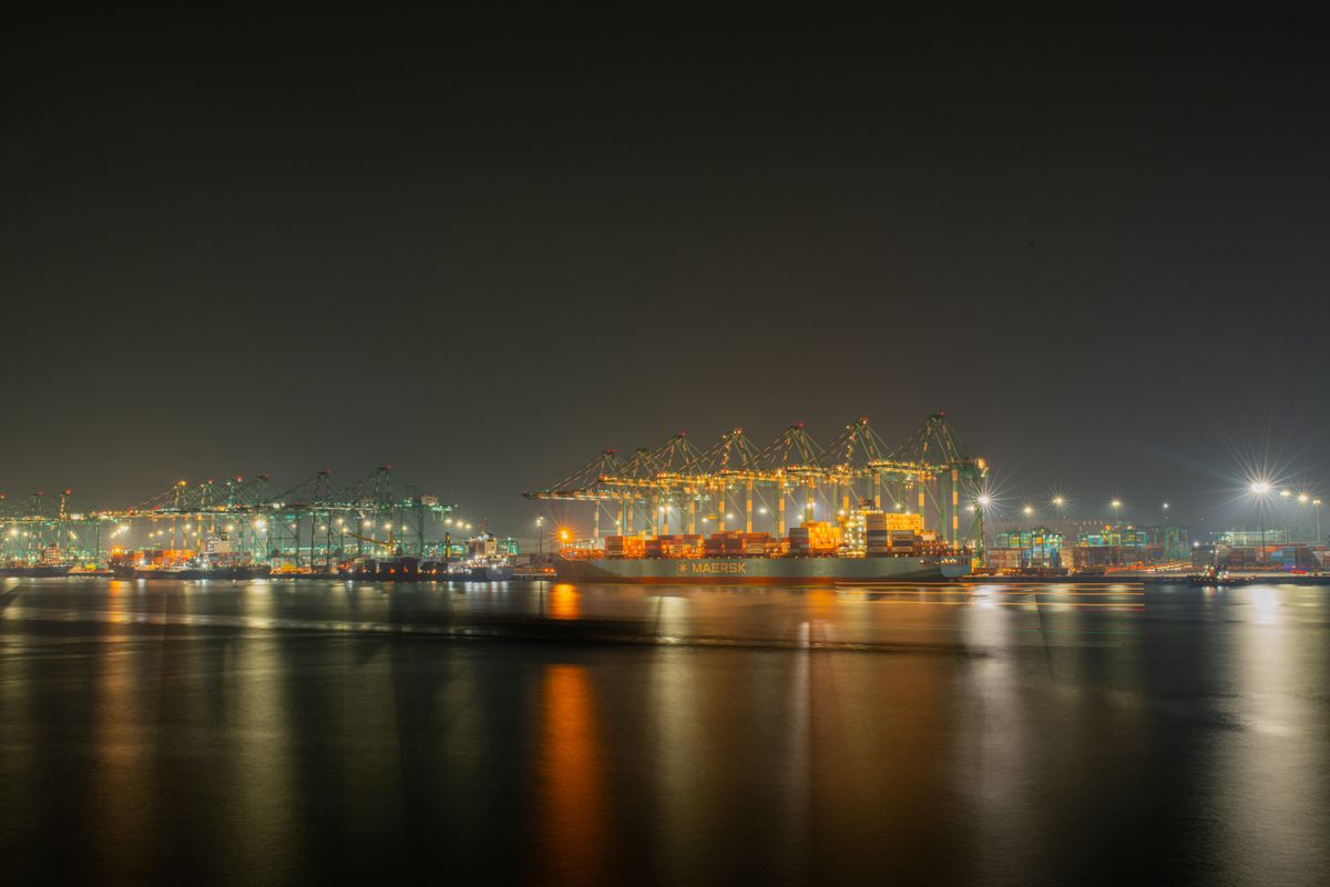 A serene nighttime view capturing the illuminated cranes and cargo ships at a bustling industrial shipping port.