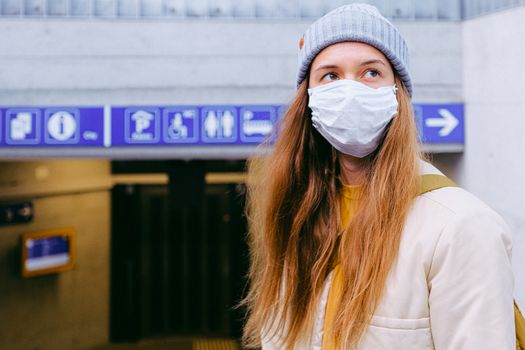 Woman in a face mask and beanie standing outdoors with signs overhead.