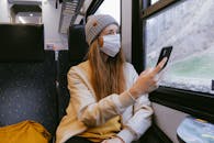 一名穿着休闲装的女子戴着口罩在火车上使用智能手机，这反映了疫情期间的生活方式