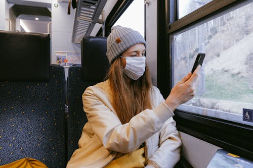 Woman in Beige Jacket and Gray Knit Cap Holding Smartphone