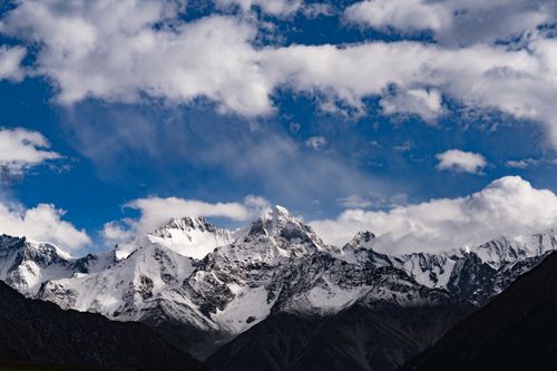 Free Stunning snow-capped mountains beneath a vibrant blue sky with fluffy clouds. Perfect for nature and travel themes. Stock Photo