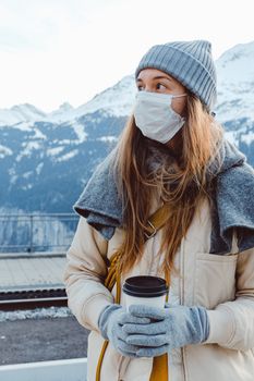 一名戴着口罩和手套的女子在雪地里拿着咖啡杯