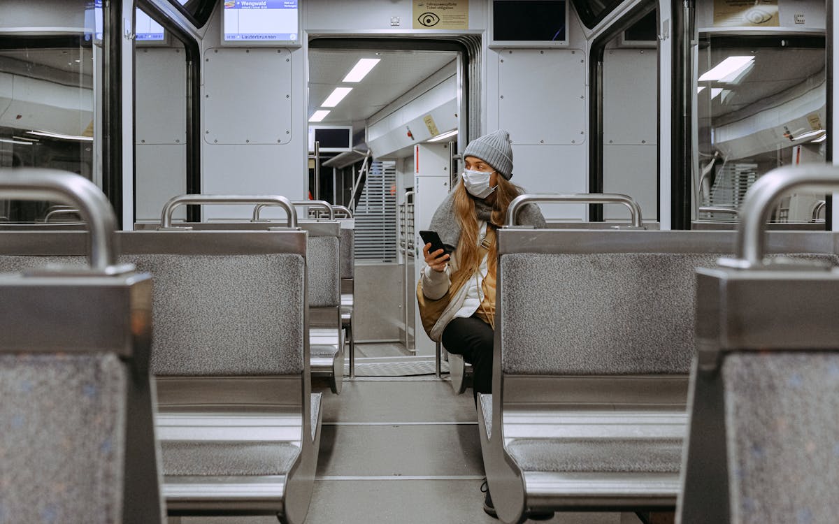 A woman wearing a face mask is sitting alone on a nearly empty urban train, practicing safety measures.