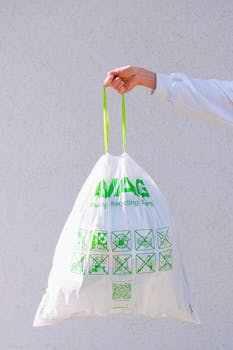 Hand holding an eco-friendly recyclable plastic bag with green symbols and labels against a white background.