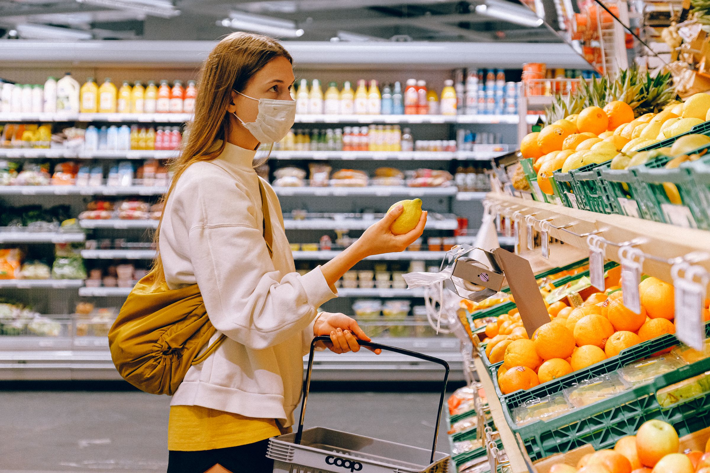 A shopper at a supermarket display, holding a piece of fruit and deciding