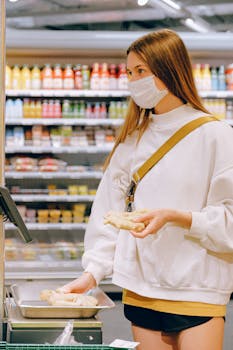 Young woman in face mask weighing ginger at supermarket, practicing safety measures.