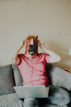 A man wearing a horse mask works on a laptop at home, blending humor with everyday life.
