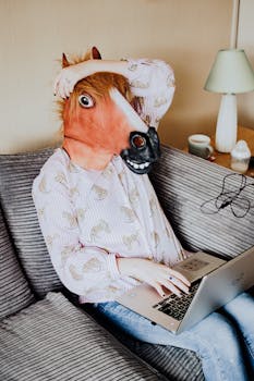 Person in a horse mask using a laptop, adding humor to remote work setting.
