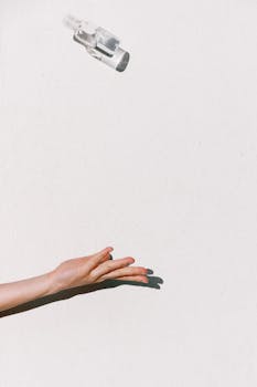 Hand tossing a sanitizer bottle midair against a white backdrop, highlighting hygiene and prevention.