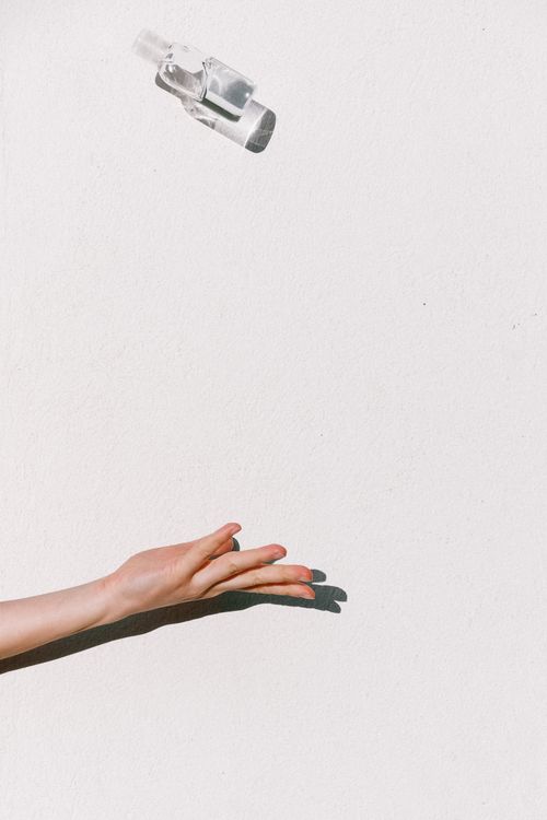 Free Hand tossing a sanitizer bottle midair against a white backdrop, highlighting hygiene and prevention. Stock Photo