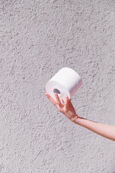 A close-up of a hand holding a toilet paper roll against a textured wall background. Minimalist and abstract style.