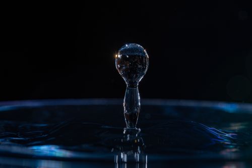 Free Close-up view of a water drop captured mid-splash with light refraction, showcasing high-speed macro photography. Stock Photo