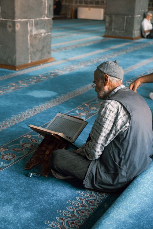 Free Senior man reading religious text in a peaceful mosque setting, emphasizing devotion and tradition. Stock Photo