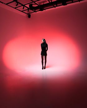 A woman stands in a dramatic red spotlight in a studio, conveying elegance and mystery.