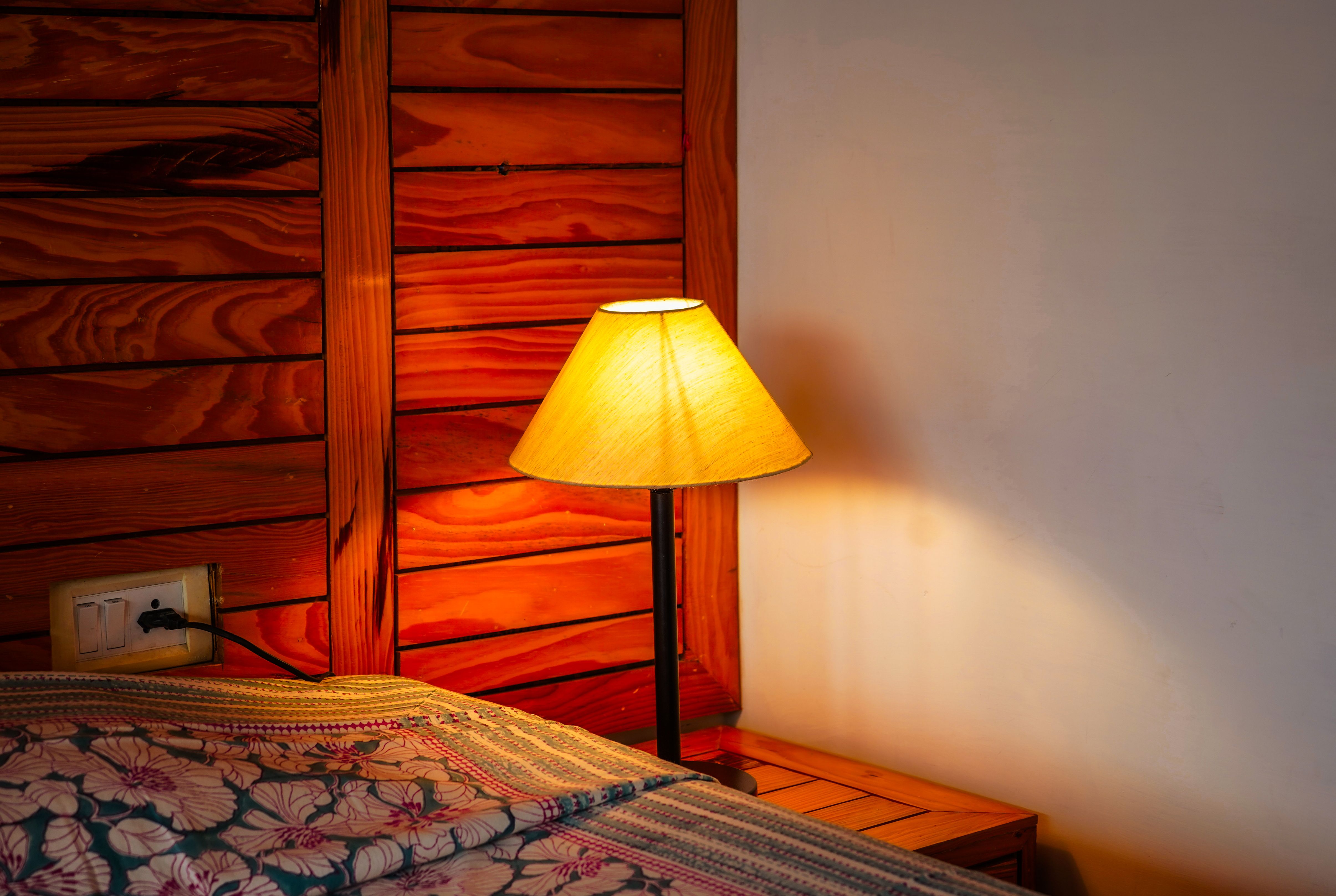 Warmly lit bedroom corner with a glowing lamp and wooden paneling.