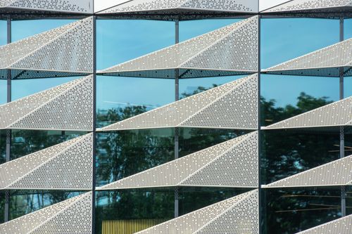 Free Close-up of a modern building facade featuring geometric patterns and glass reflection. Stock Photo