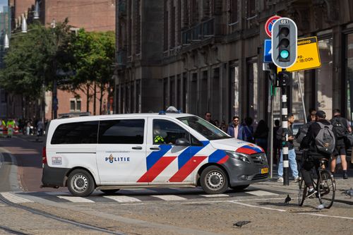 Free A Dutch police van navigates a busy city intersection, surrounded by pedestrians and cyclists. Stock Photo