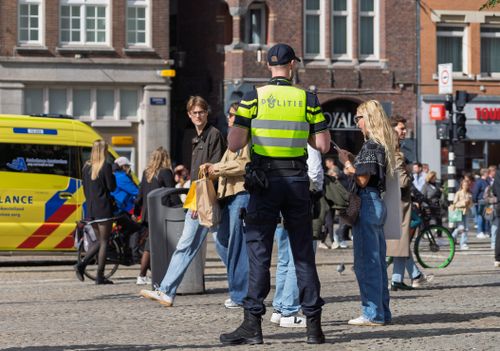 Free Police officer interacting with people in Amsterdam city center during daytime. Stock Photo