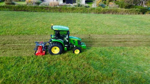 Free Aerial shot of green tractor mowing a lush rural field, highlighting agriculture. Stock Photo