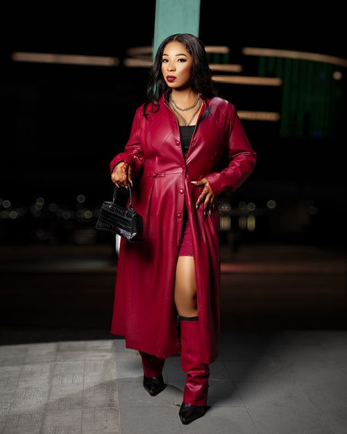 Free Elegant woman in a red leather coat poses confidently against a city night backdrop. Stock Photo