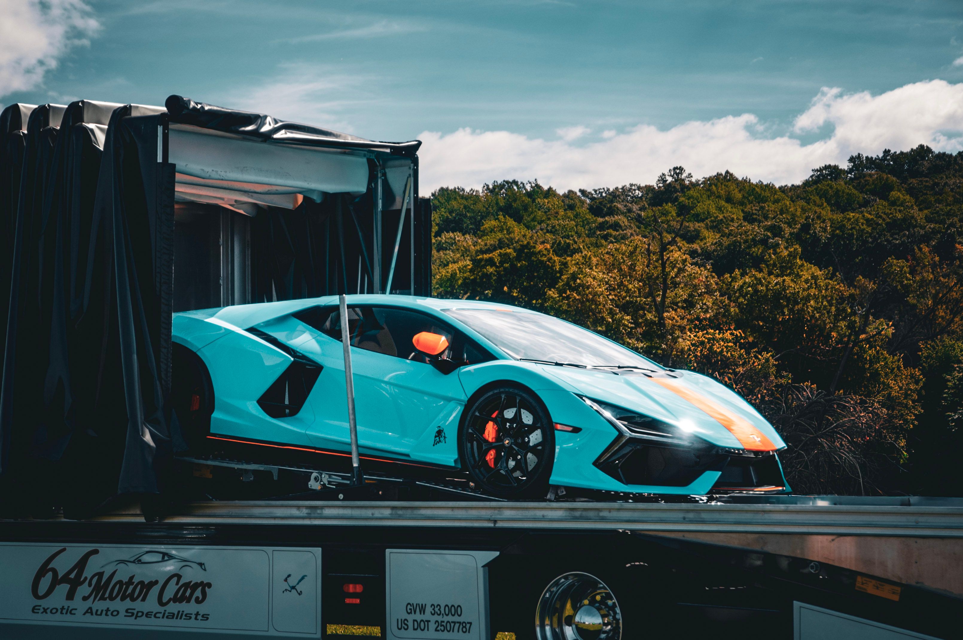 A luxury sports car is loaded onto a trailer for transport amidst a scenic outdoor setting.