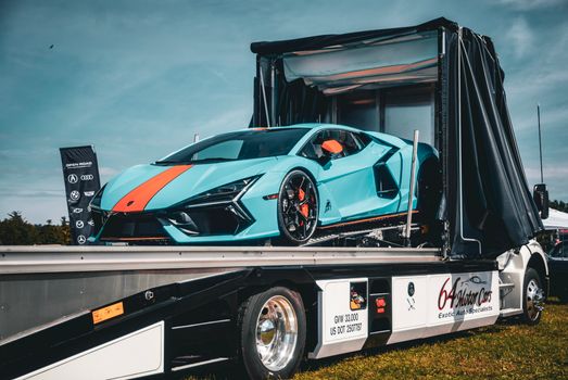 A striking blue Lamborghini sports car showcased on a transport truck in an outdoor setting.