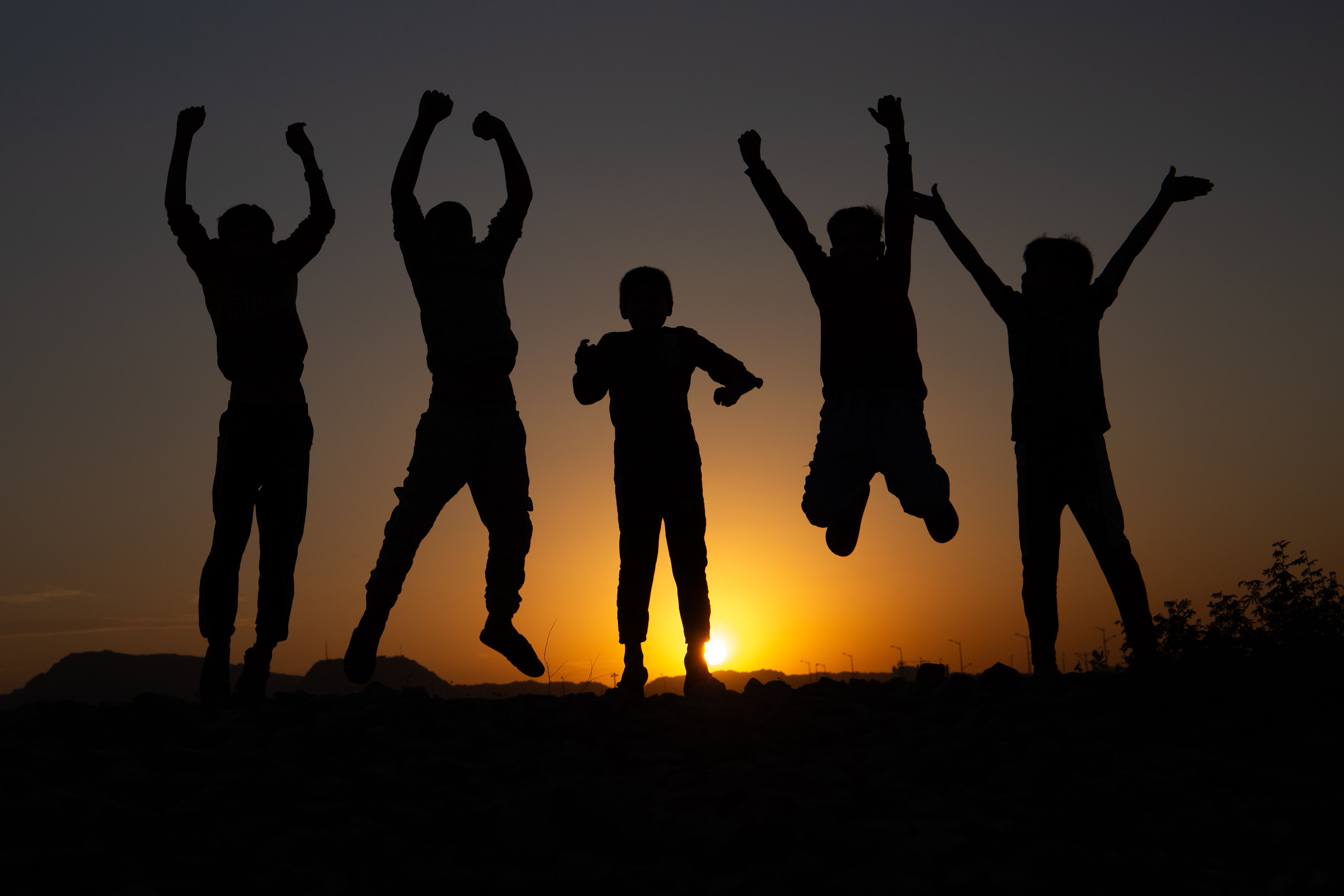 Excited group of children jumping in silhouette against a stunning sunset backdrop, capturing pure joy.
