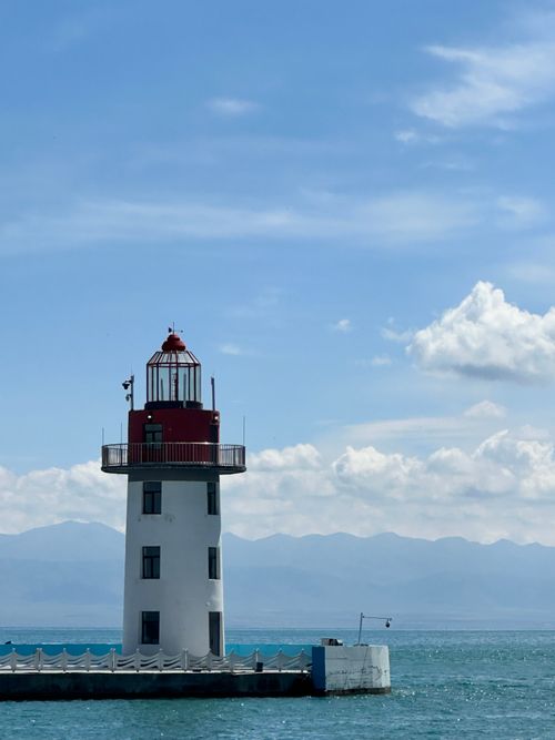 Free White and red lighthouse by the clear blue waters of Qinghai Lake, set against distant mountains under a bright sky. Stock Photo