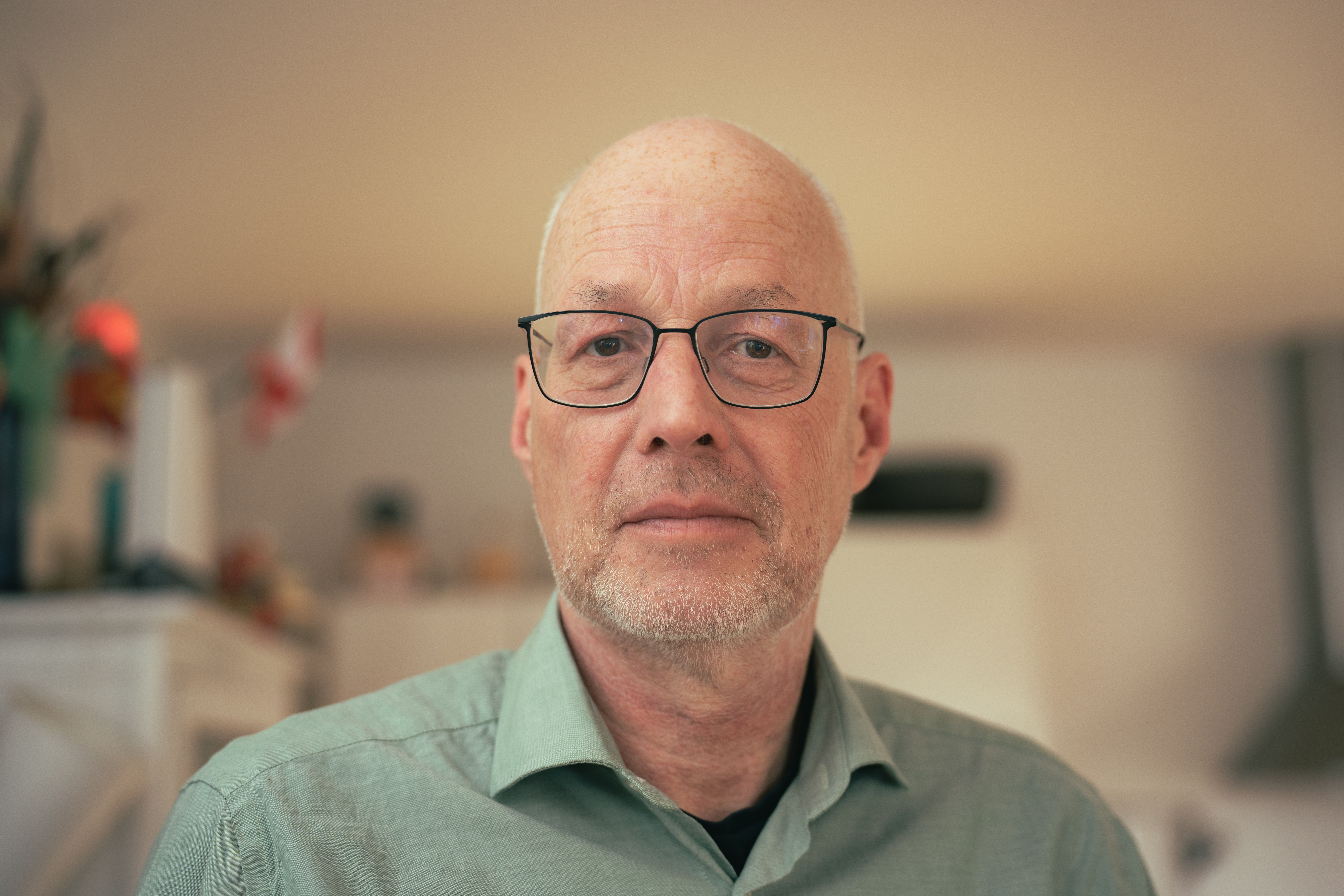 Close-up portrait of a mature man with glasses indoors, soft lighting adds warmth.