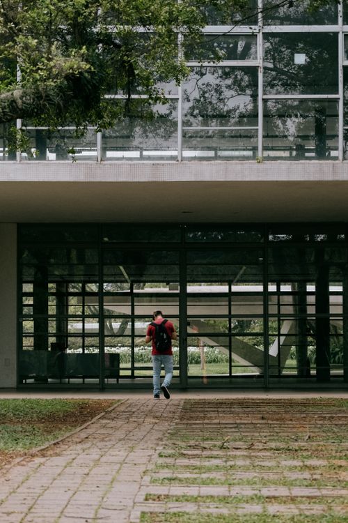 Free Lone student with a red backpack entering glass building on São Paulo campus. Stock Photo