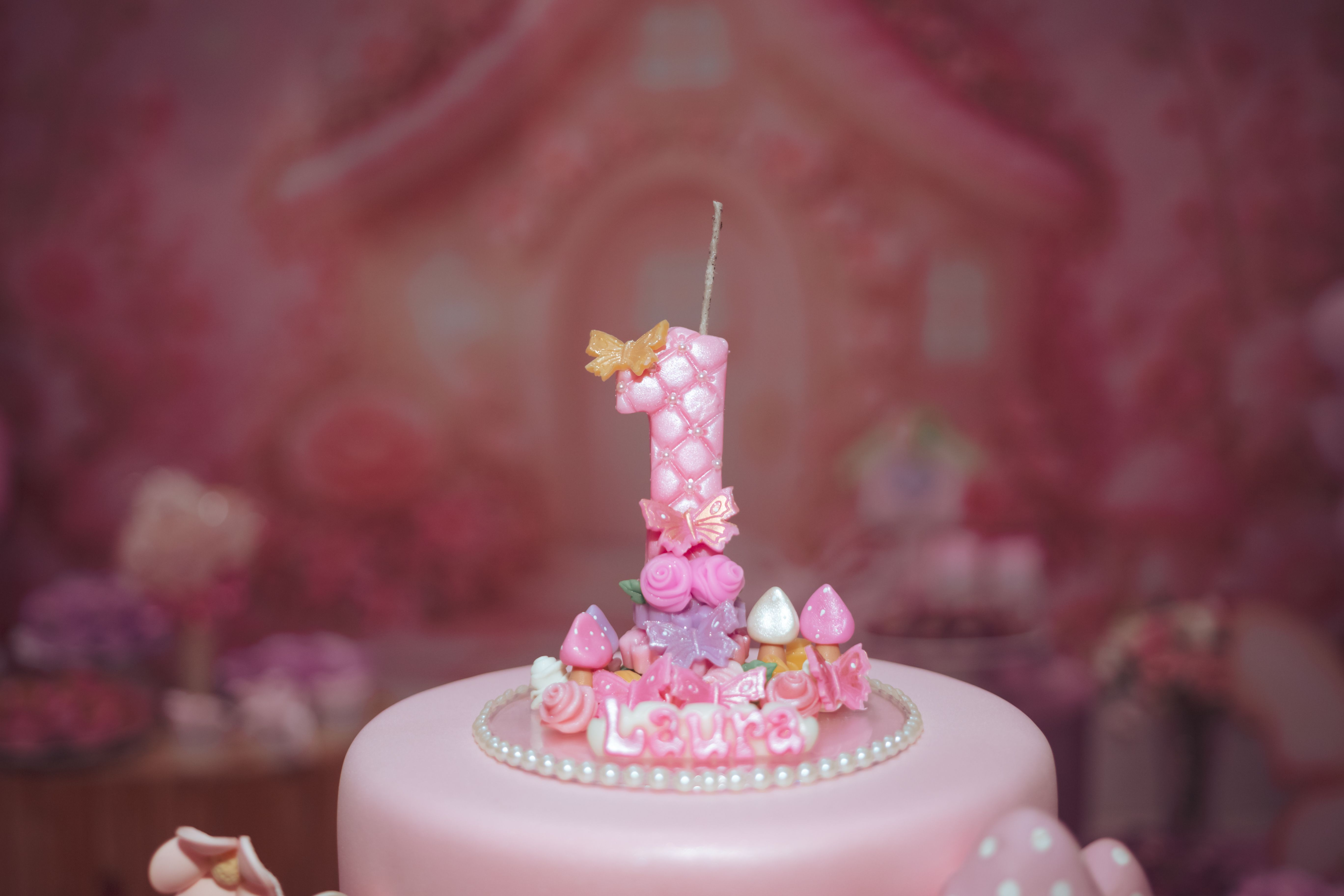 Pink birthday cake decorated with a number-one candle and the name Laura