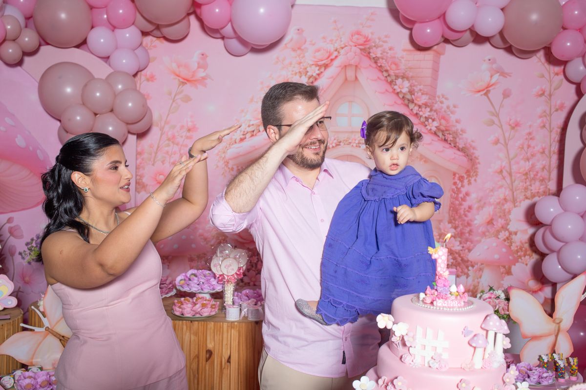Joyful family celebrating a first birthday with balloons and a cake in a pastel-themed party. Stock Photo.