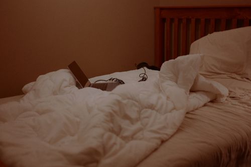 Free A cozy bedroom with a laptop and headphones on a white comforter, creating a relaxed ambiance. Stock Photo