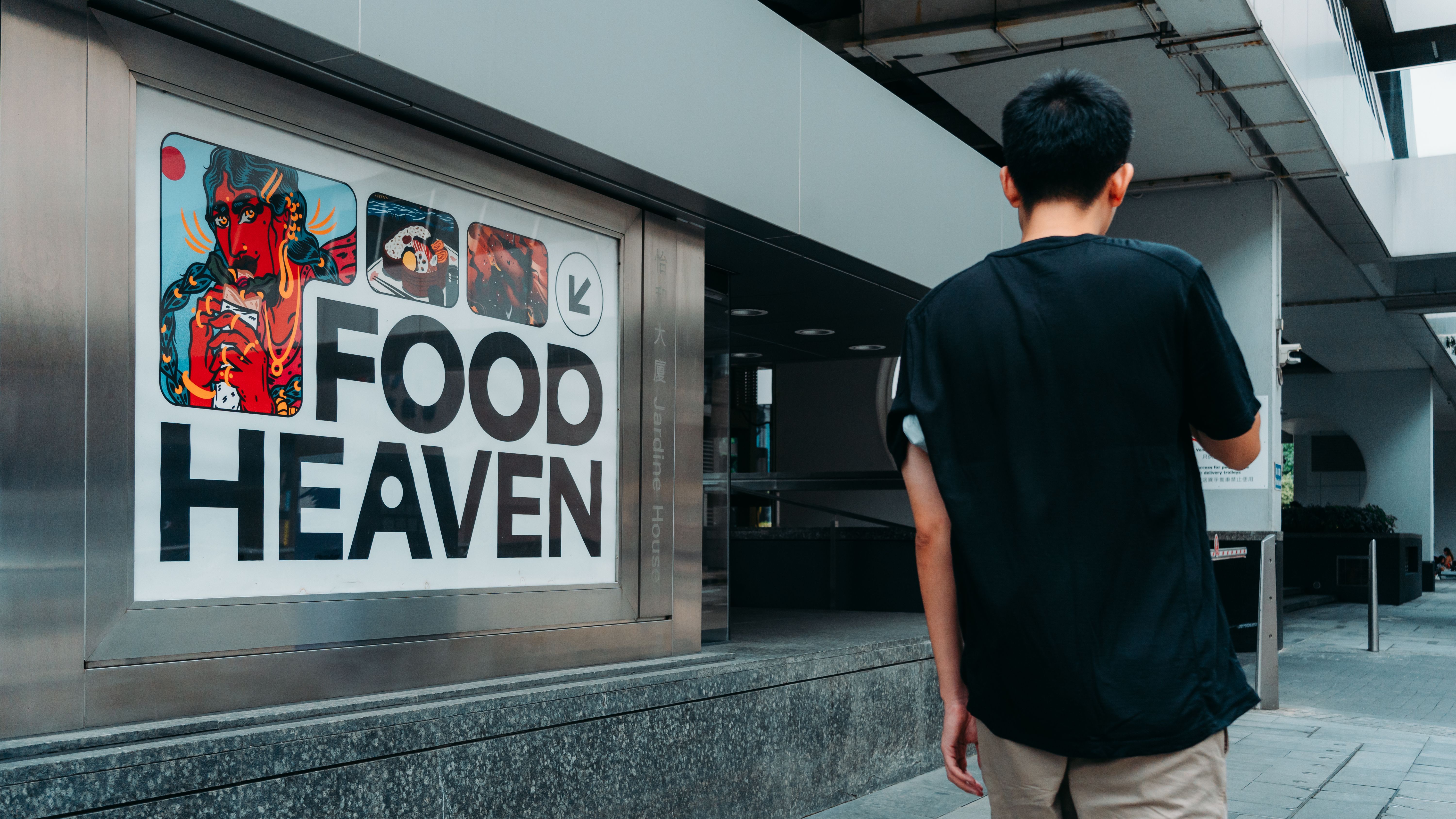 Man walking towards a colorful 'Food Heaven' sign in a modern urban setting.