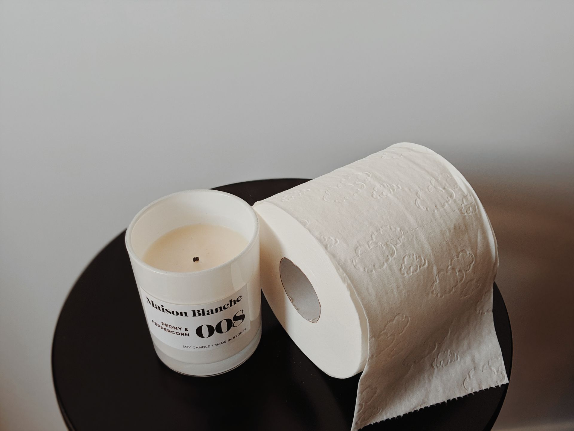 A clean, minimalist setup featuring a scented candle and toilet paper roll on a black surface.