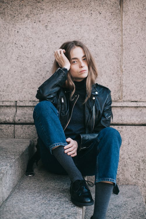 Woman in Blue Denim Jacket and Blue Denim Jeans Sitting on Gray Concrete Stairs