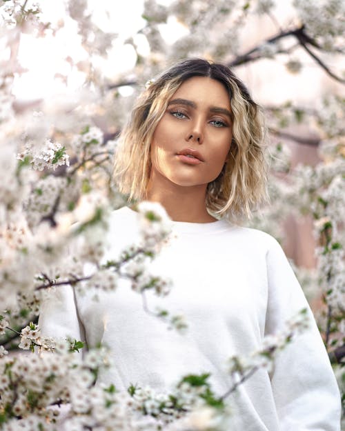 Free Woman In White Crew Neck Sweater Standing Near White Flowers Stock Photo