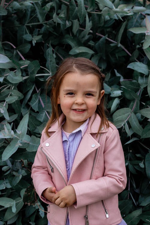 Free Girl in Pink Leather Jacket Standing Beside Green Plants Stock Photo