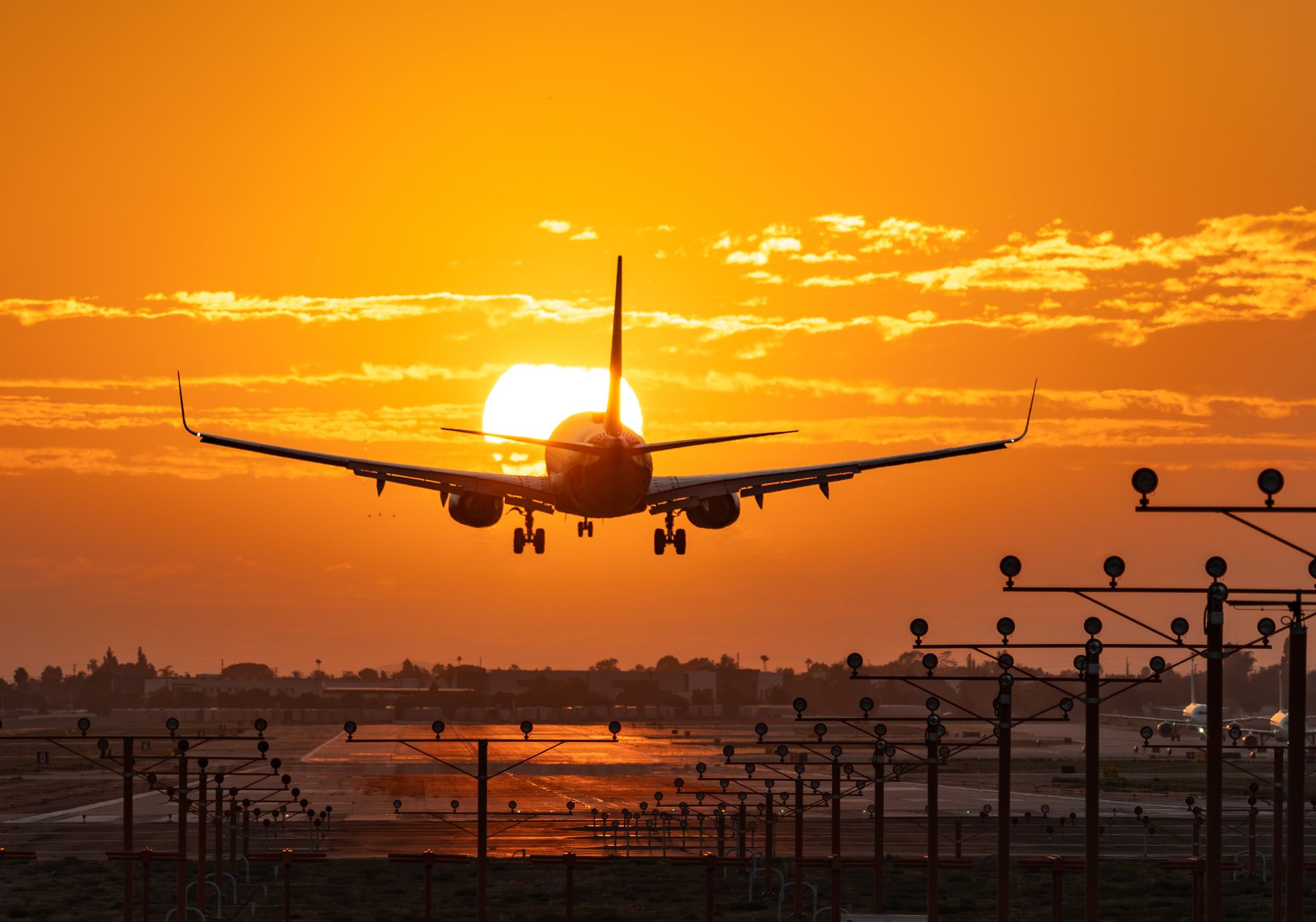 A passenger jet landing at sunset over runway approach lights