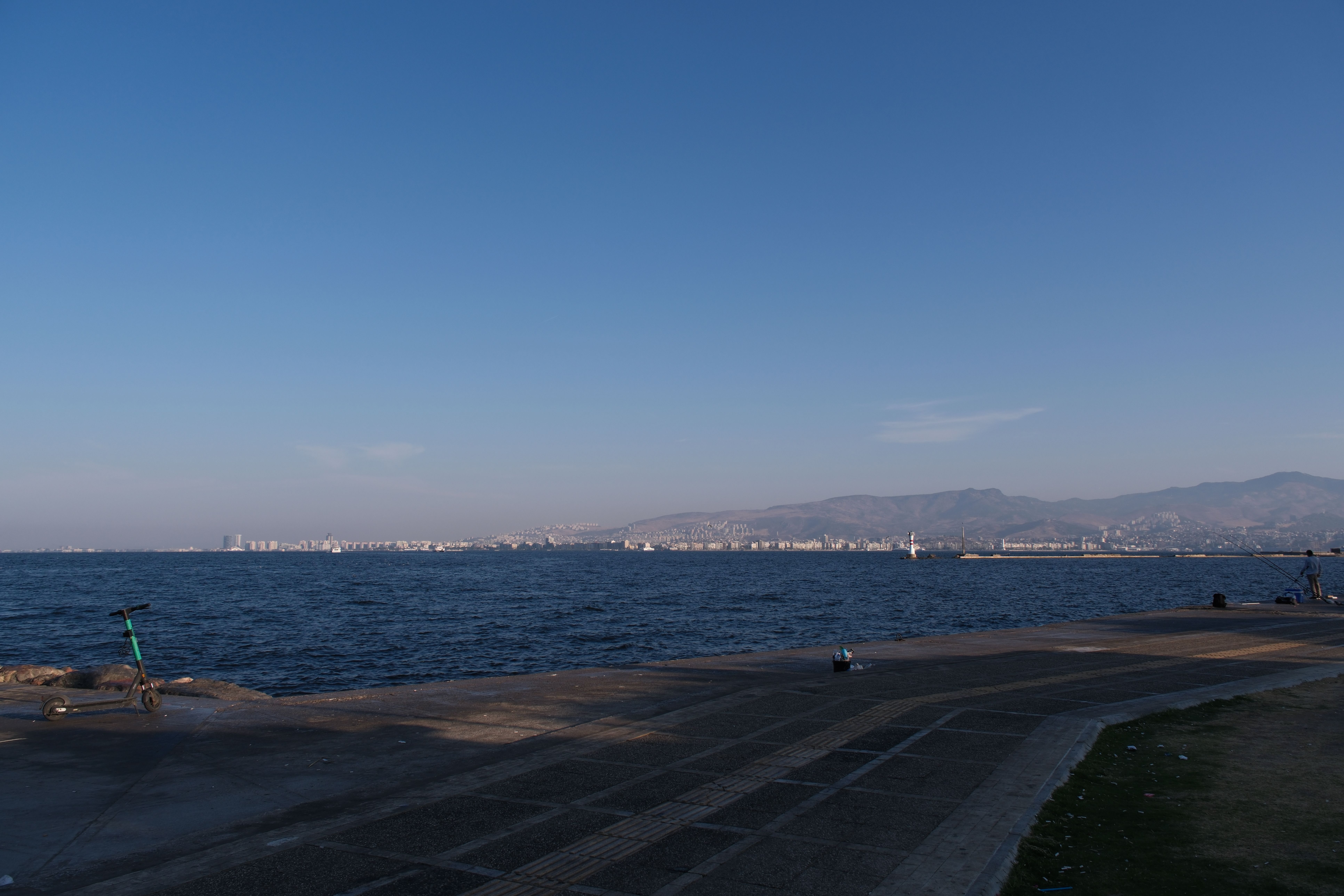 Serene view of İzmir Bay's coastline with cityscape and distant mountains under clear blue skies.