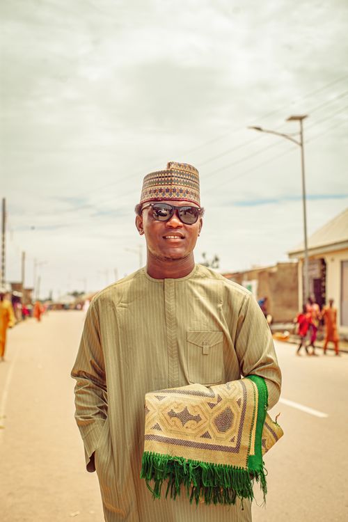 Free Man in traditional dress with a prayer mat, outdoors on a sunny day, embodying cultural pride. Stock Photo