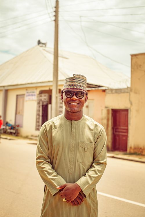 Free A cheerful man wearing traditional clothing stands outdoors in an urban setting. Stock Photo