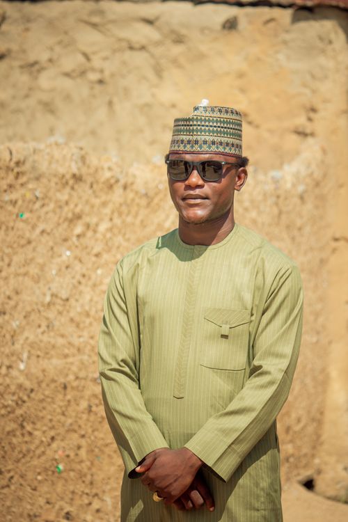 Free Man in traditional attire and sunglasses standing against earthy wall background. Stock Photo
