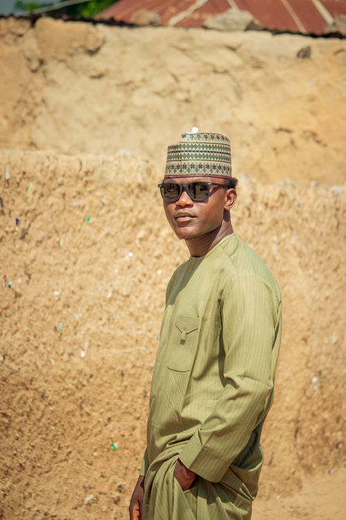 Free Man in traditional attire and hat standing outdoors against an earthy background. Stock Photo