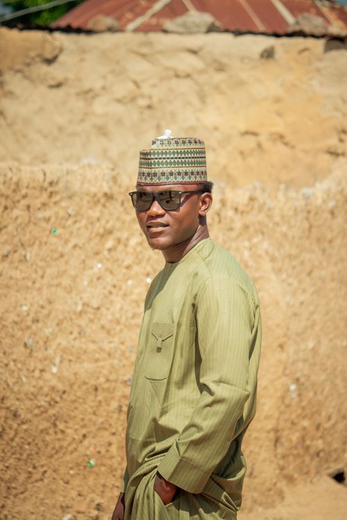 Free Man in traditional attire and sunglasses standing outdoors against an earthy backdrop. Stock Photo