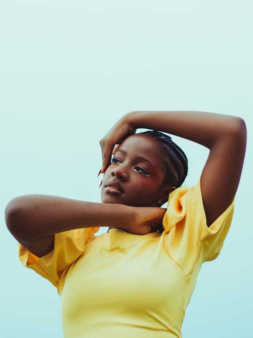 Free A serene portrait of a young woman in a yellow shirt against a pastel sky background. Stock Photo