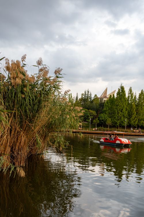 Free Picturesque view of a lake in Ankara's Anka Park. A pedal boat floats under a cloudy sky. Stock Photo