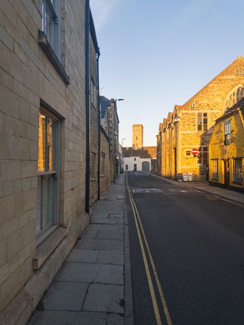 Free A peaceful street in Malmesbury, England, captured at dawn with warm sunlight on historic buildings. Stock Photo