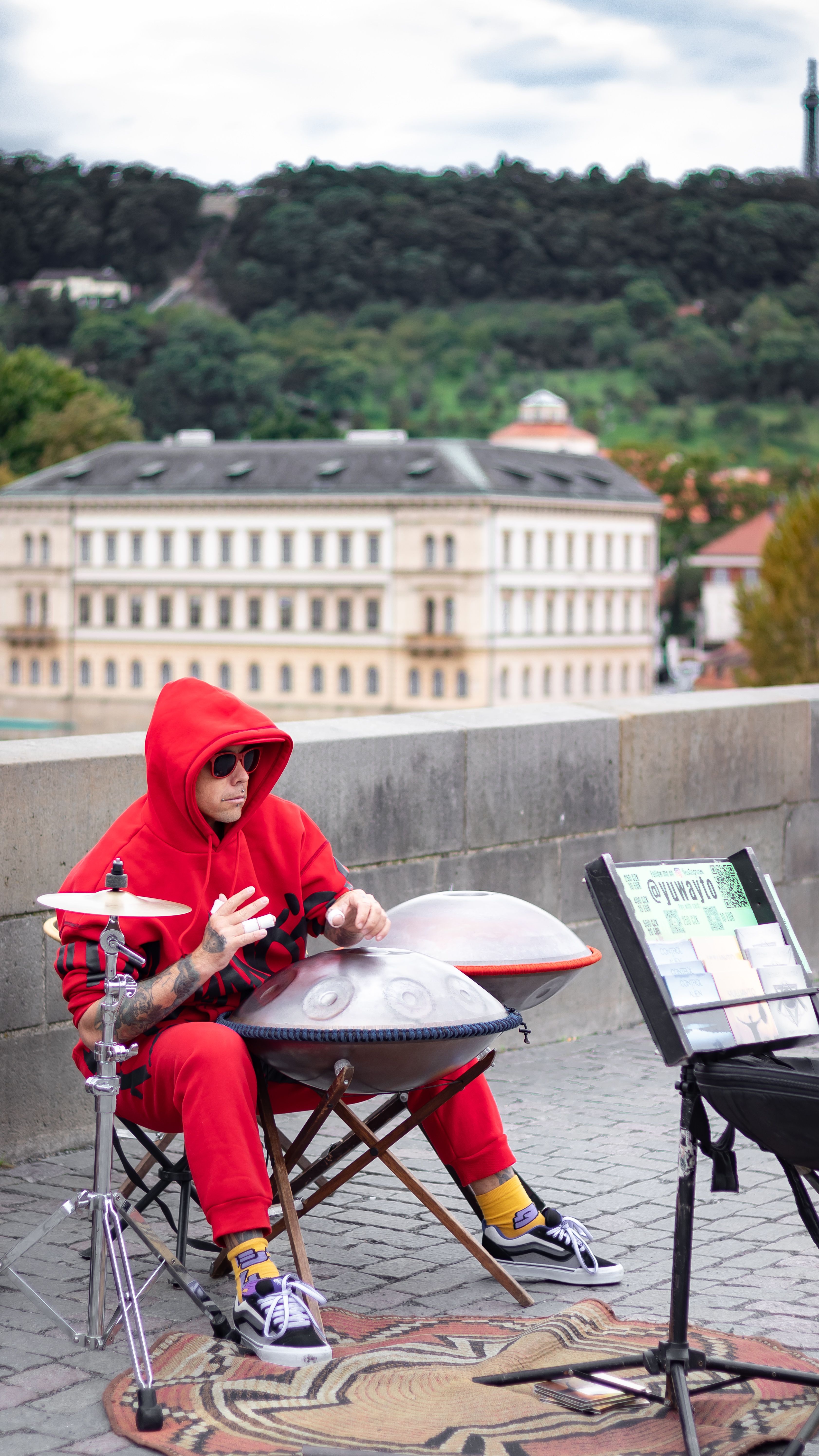 Street performer in red outfit plays handpan on a public square in urban setting, capturing a lively atmosphere.