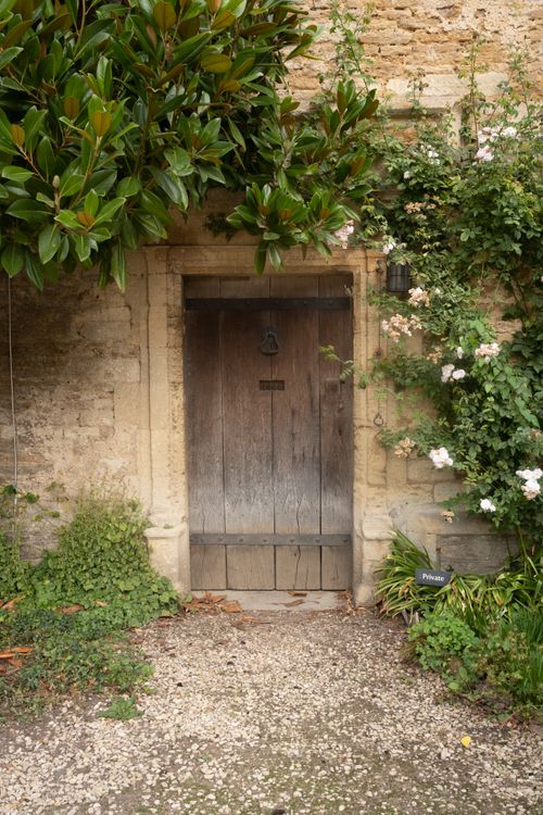 Free A rustic wooden door surrounded by lush greenery and quaint stone walls in Lacock, England. Stock Photo